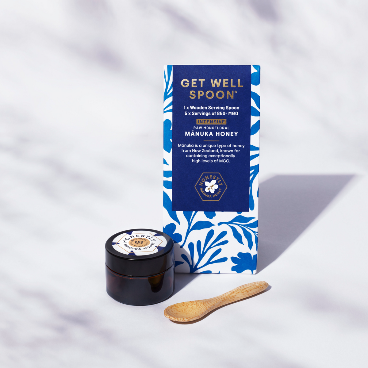 Manuka honey jar with packaging and wooden spoon on a white background