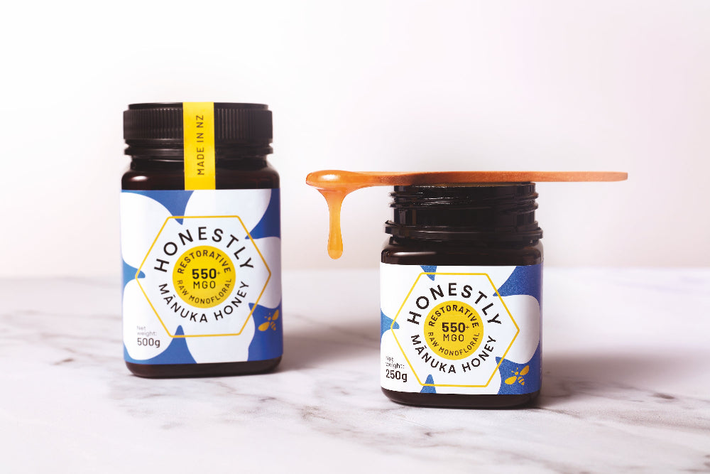 Two jars of 'Honestly' Manuka Honey on a marble surface with a white background