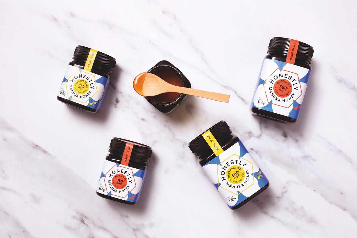 Five jars of 'Honestly Honey' on a marble surface with a wooden spoon.